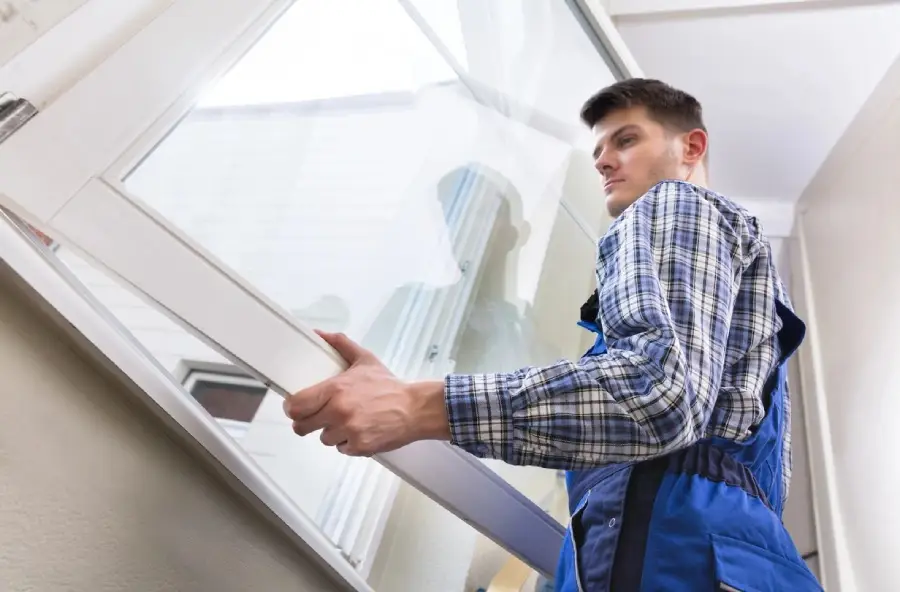 A man in blue overalls is holding a window