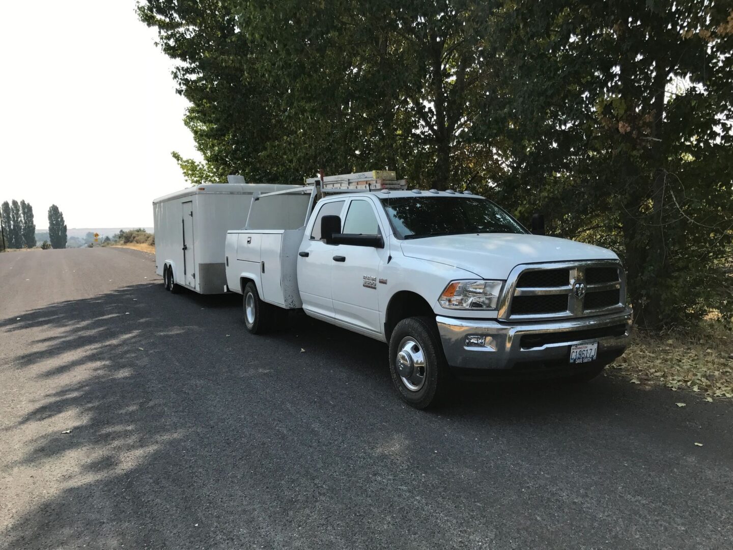 A white truck and trailer on the side of the road.